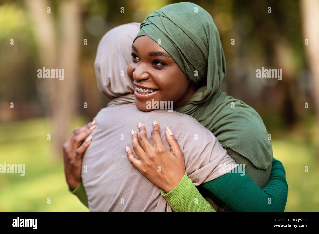 Two Diverse Islamic Ladies Embracing Standing In Park Outside Stock Photo