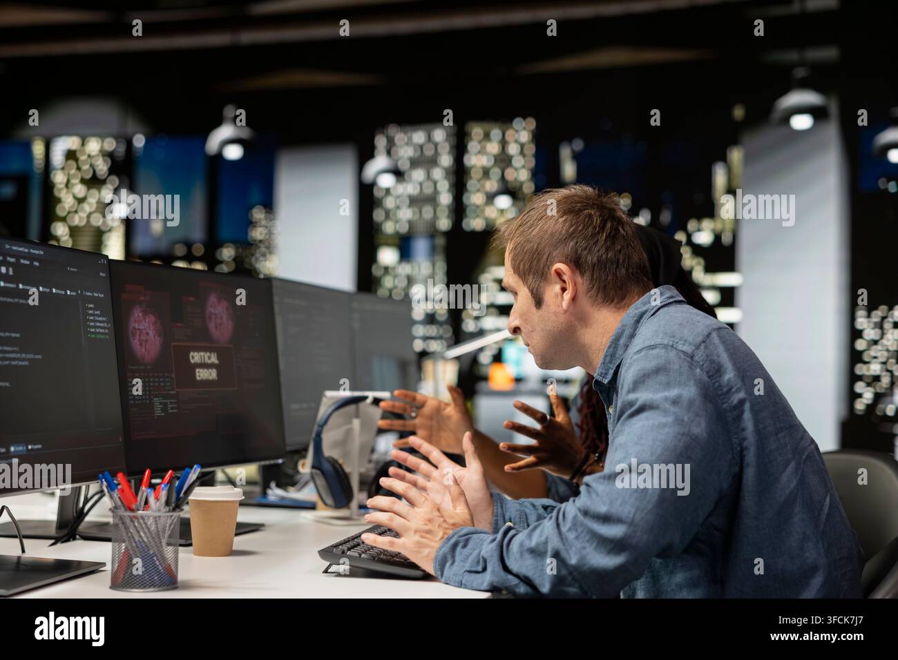 Software developer at office desk thinking how to fix critical error warning displayed on computer. Tech startup IT worker brainstorming how to fix co Stock Photo