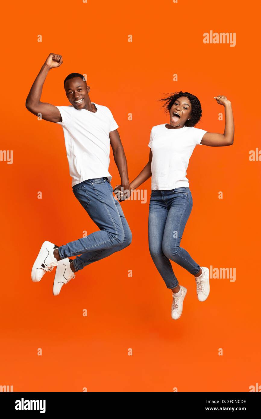 Emotional black couple holding hands and jumping up Stock Photo
