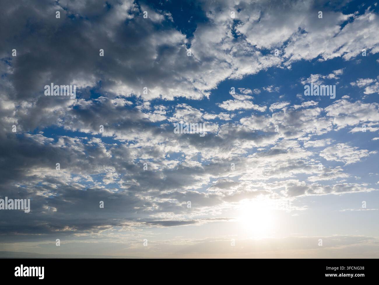Sunlight pierces through scattered clouds on vast blue sky Stock Photo