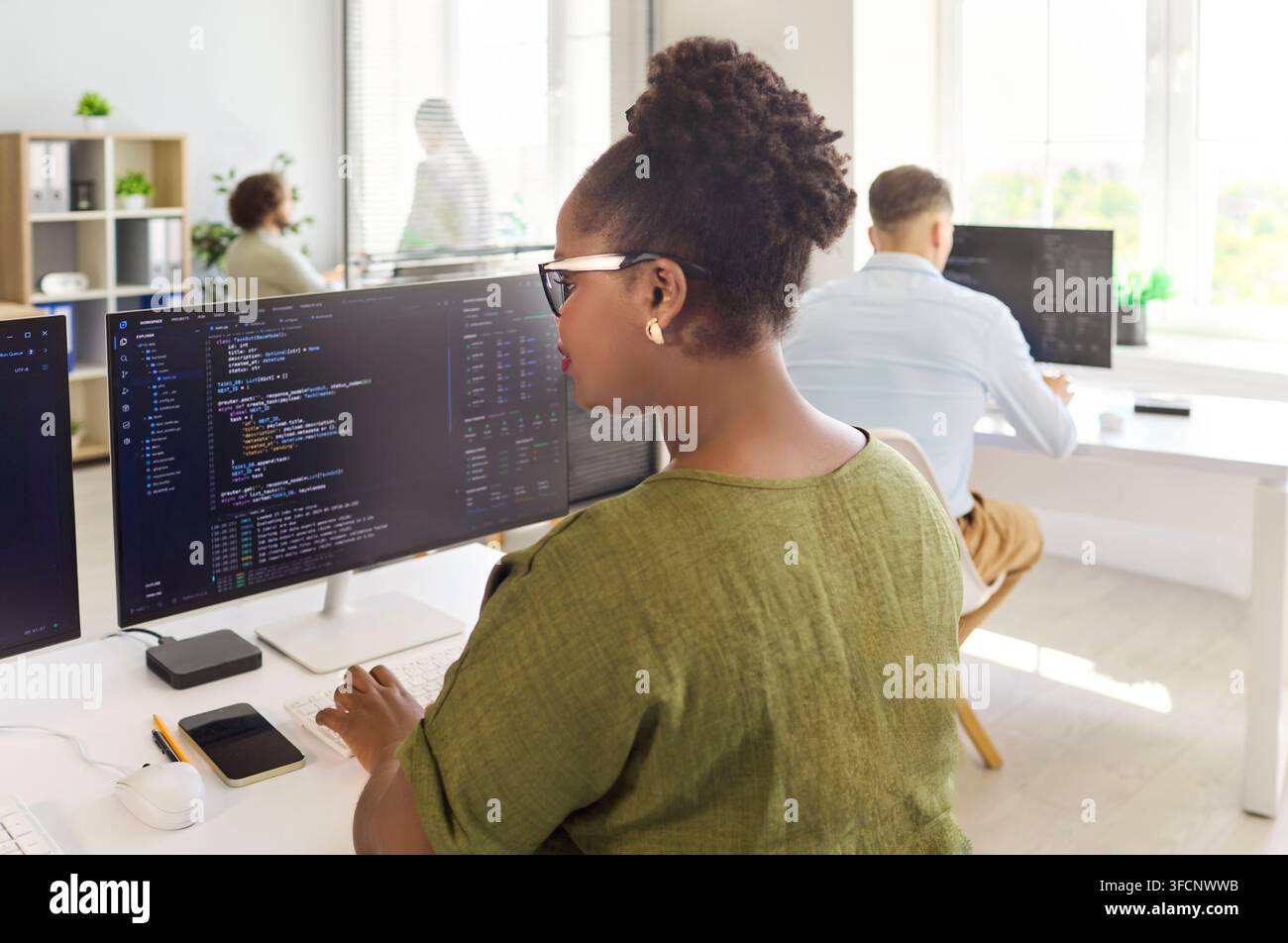 Programmers collaborating at modern office desks with code on dual monitors Stock Photo