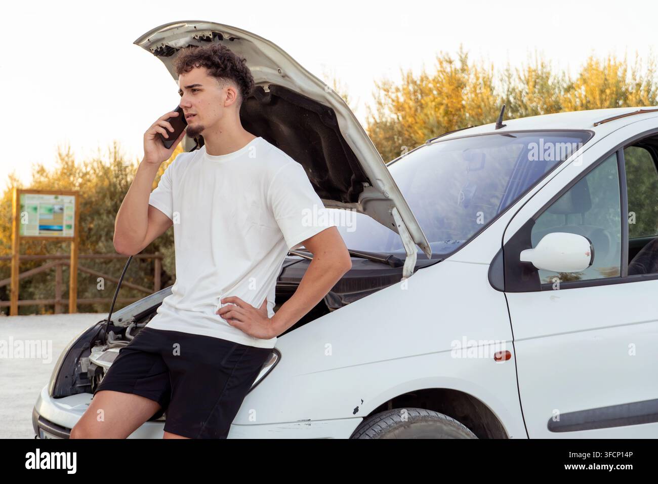 Young man using a smartphone, calling for help with his broken-down car, experiencing vehicle engine trouble Stock Photo
