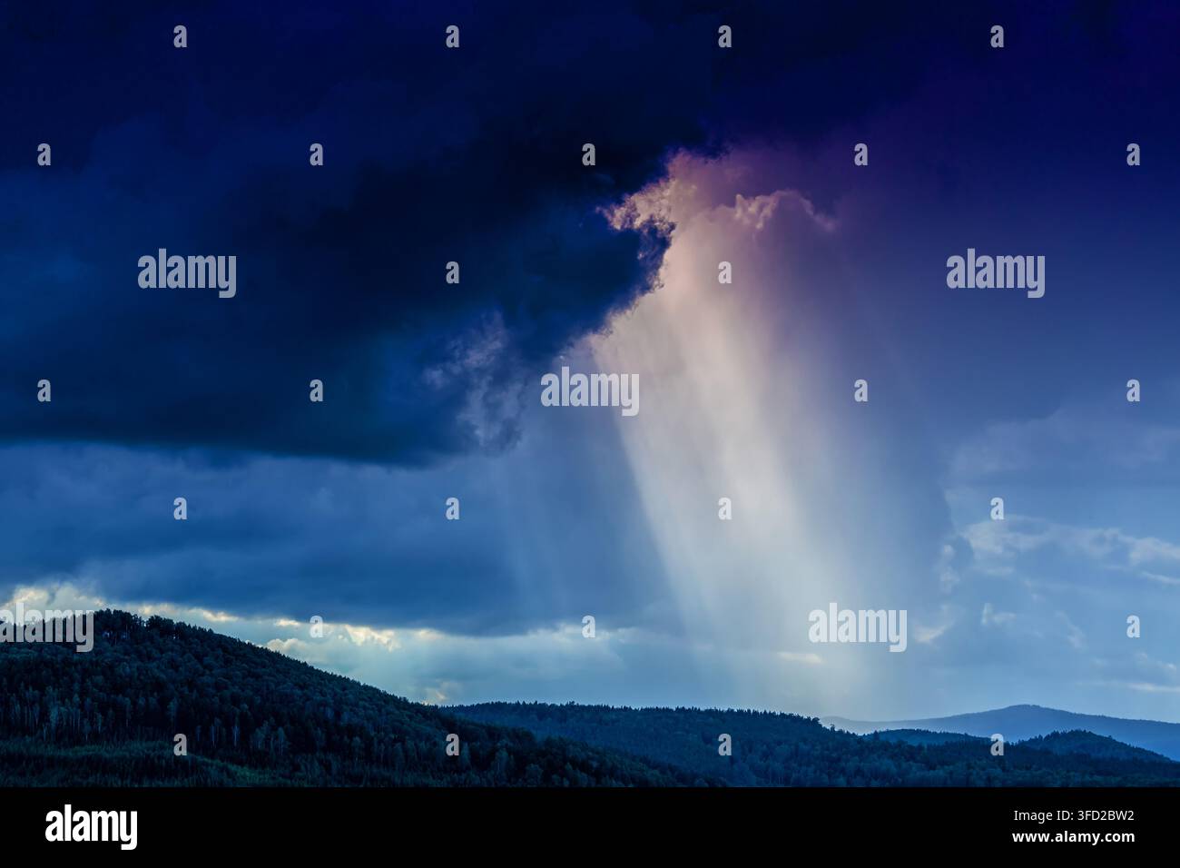 Dramatic sun rays breaking through storm clouds over mountain forest Stock Photo
