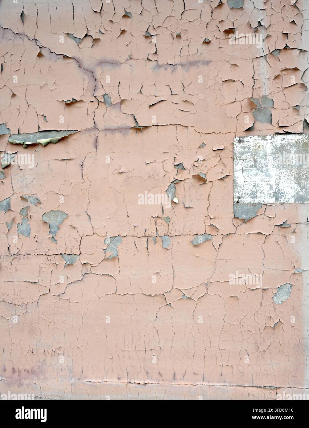 Weathered tan painted concrete wall in vertical close-up with cracked peeling paint, exposed cement, chipped white painted rectangle Stock Photo