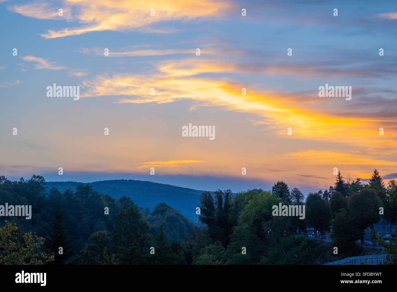 Dramatic sunset sky glowing above forested hills and valley Stock Photo