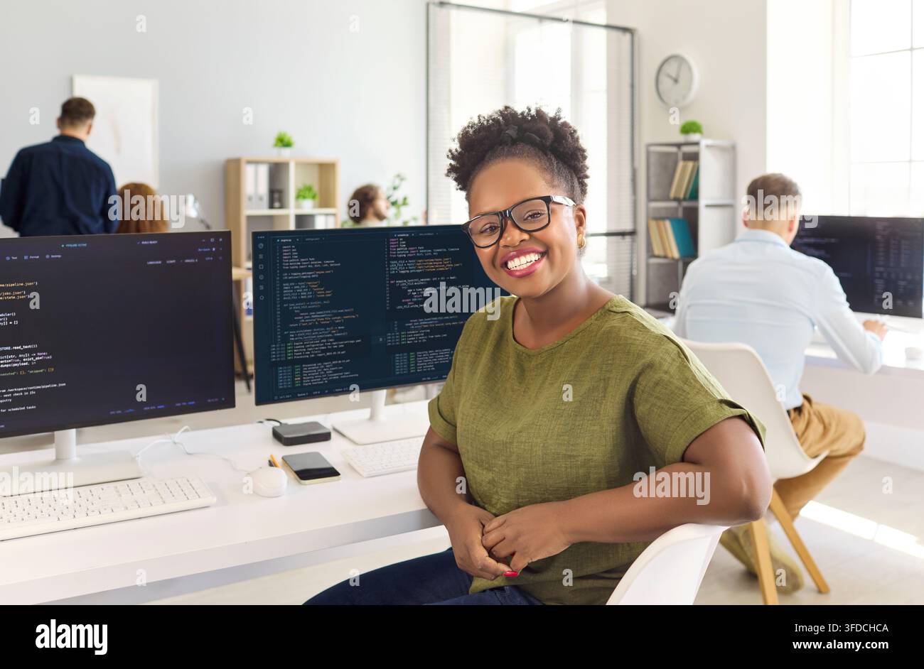 Happy woman programmer at computer workstation in bright office with code screens Stock Photo