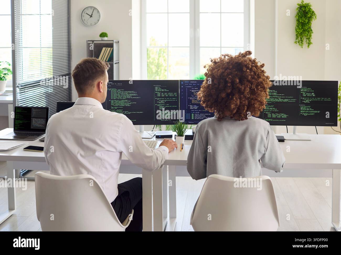 Developers pair programming at multi monitor workstation in modern bright office Stock Photo