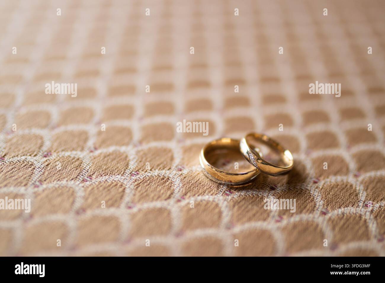 Two gold wedding rings sit on patterned fabric Stock Photo