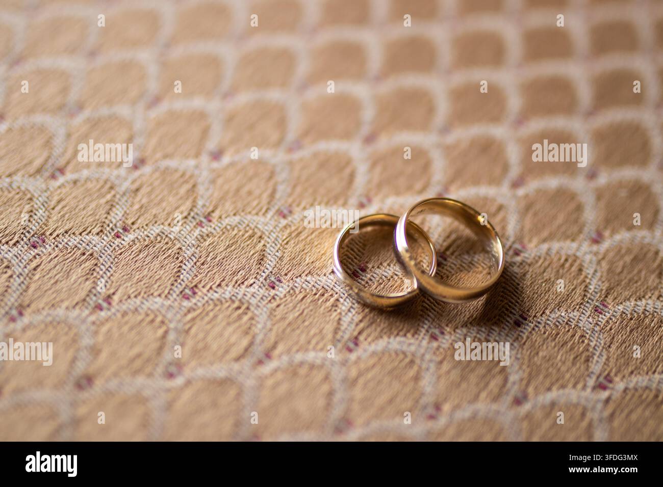 Two gold wedding bands resting on patterned fabric Stock Photo