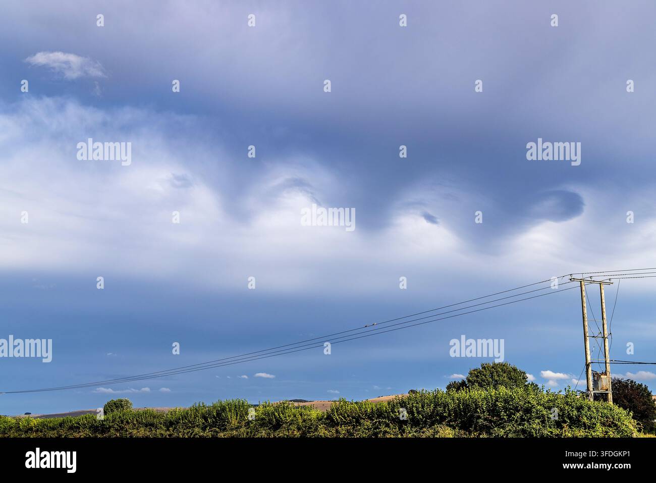 Dramatic undulating storm clouds forming wave like patterns above a rural landscape. Stock Photo