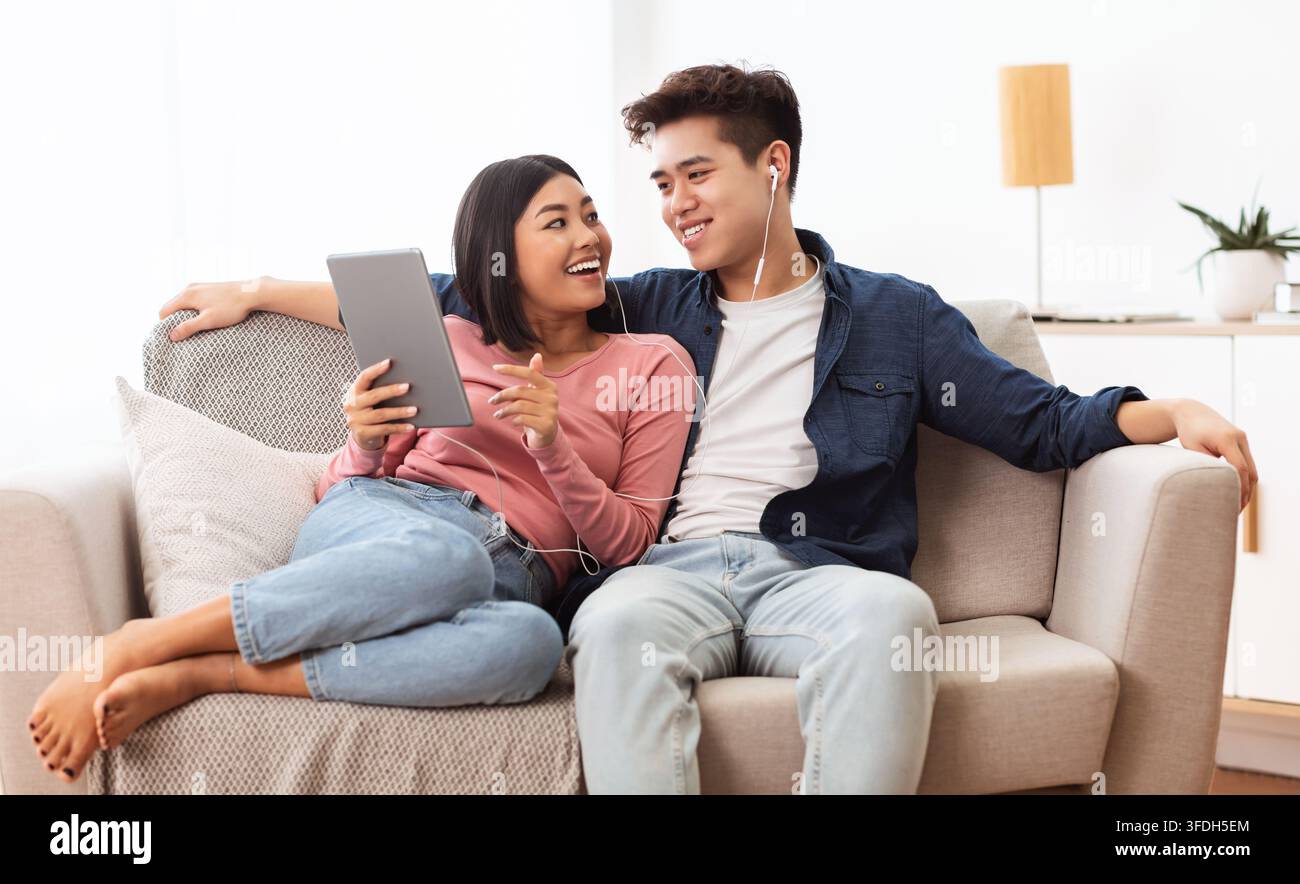Japanese Spouses Using Tablet Browsing Internet Sitting On Couch Indoor Stock Photo