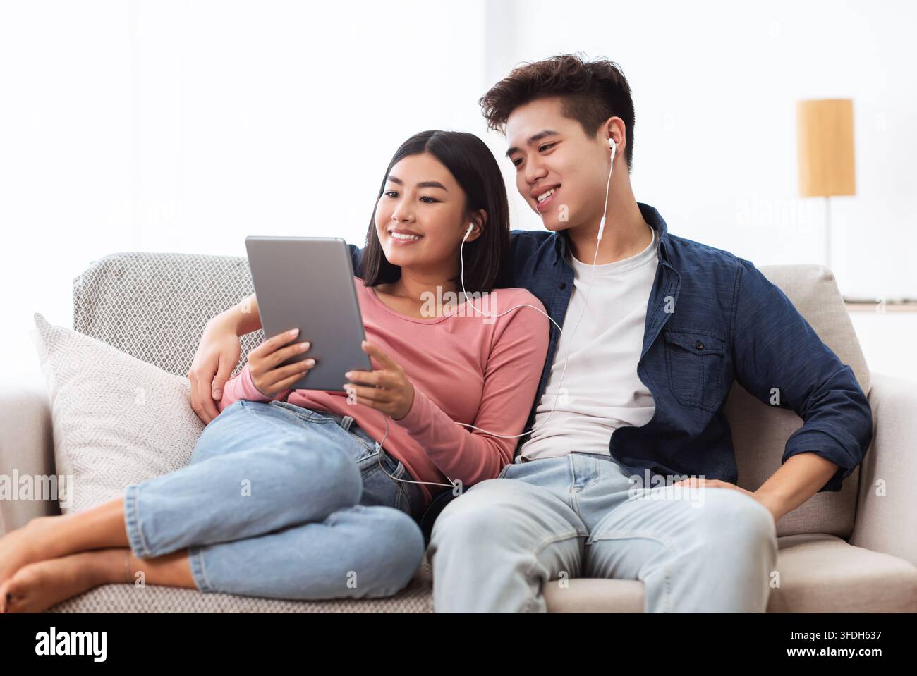 Cheerful Korean Couple Using Digital Tablet Computer Sitting At Home Stock Photo