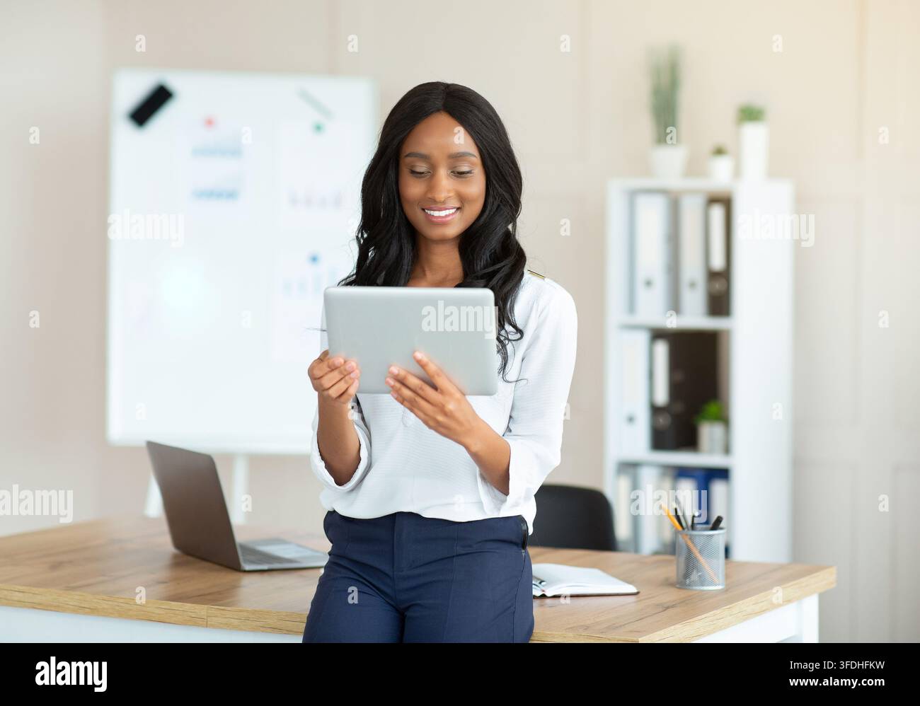 Joyful black lady using tablet pc, searching info on web at modern office Stock Photo