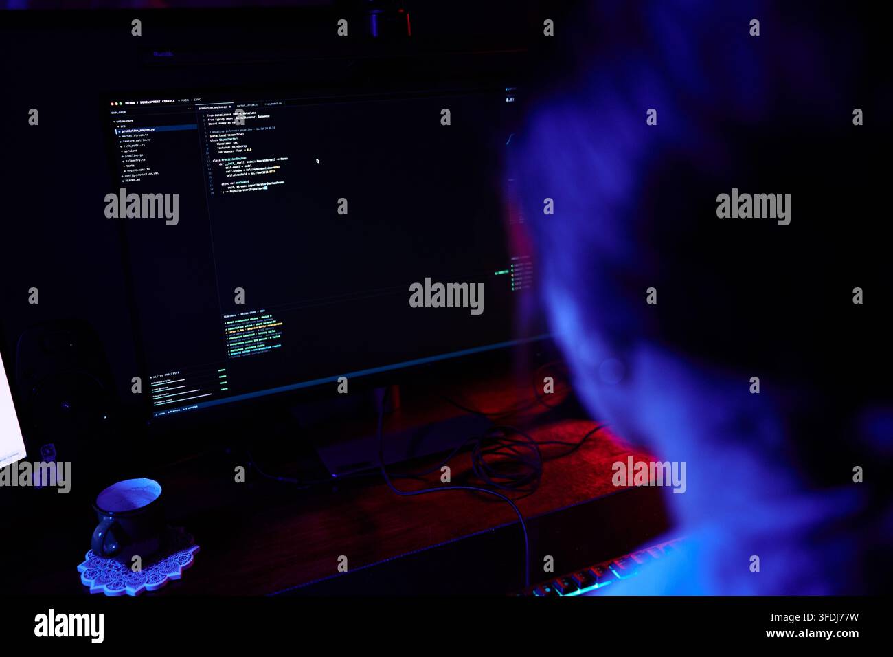 Person programming code on computer screen in dark room, representing cybersecurity, hacking, and software development Stock Photo