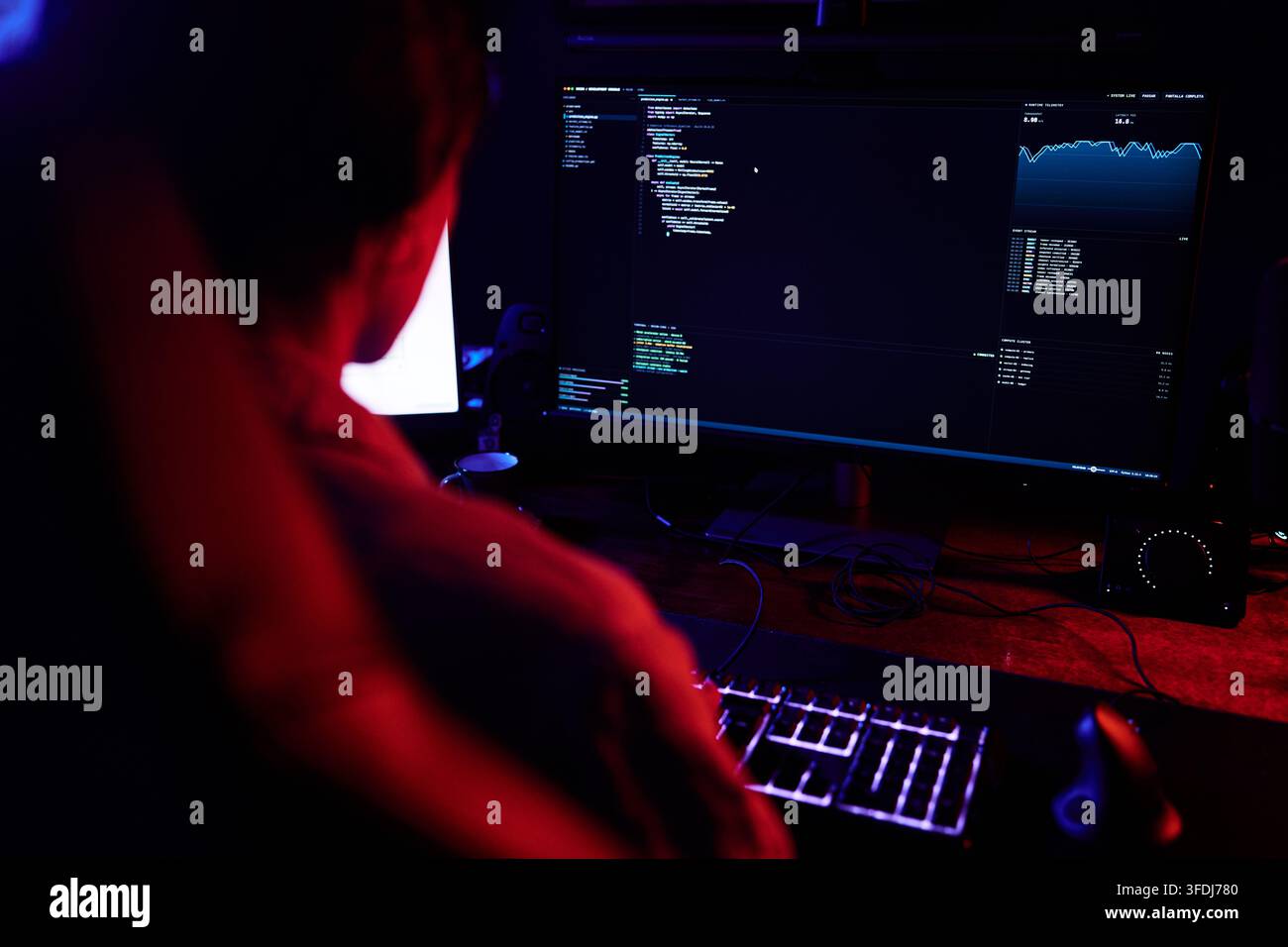 Hacker working in a dark room, typing code on a backlit keyboard, creating software or breaking into systems Stock Photo