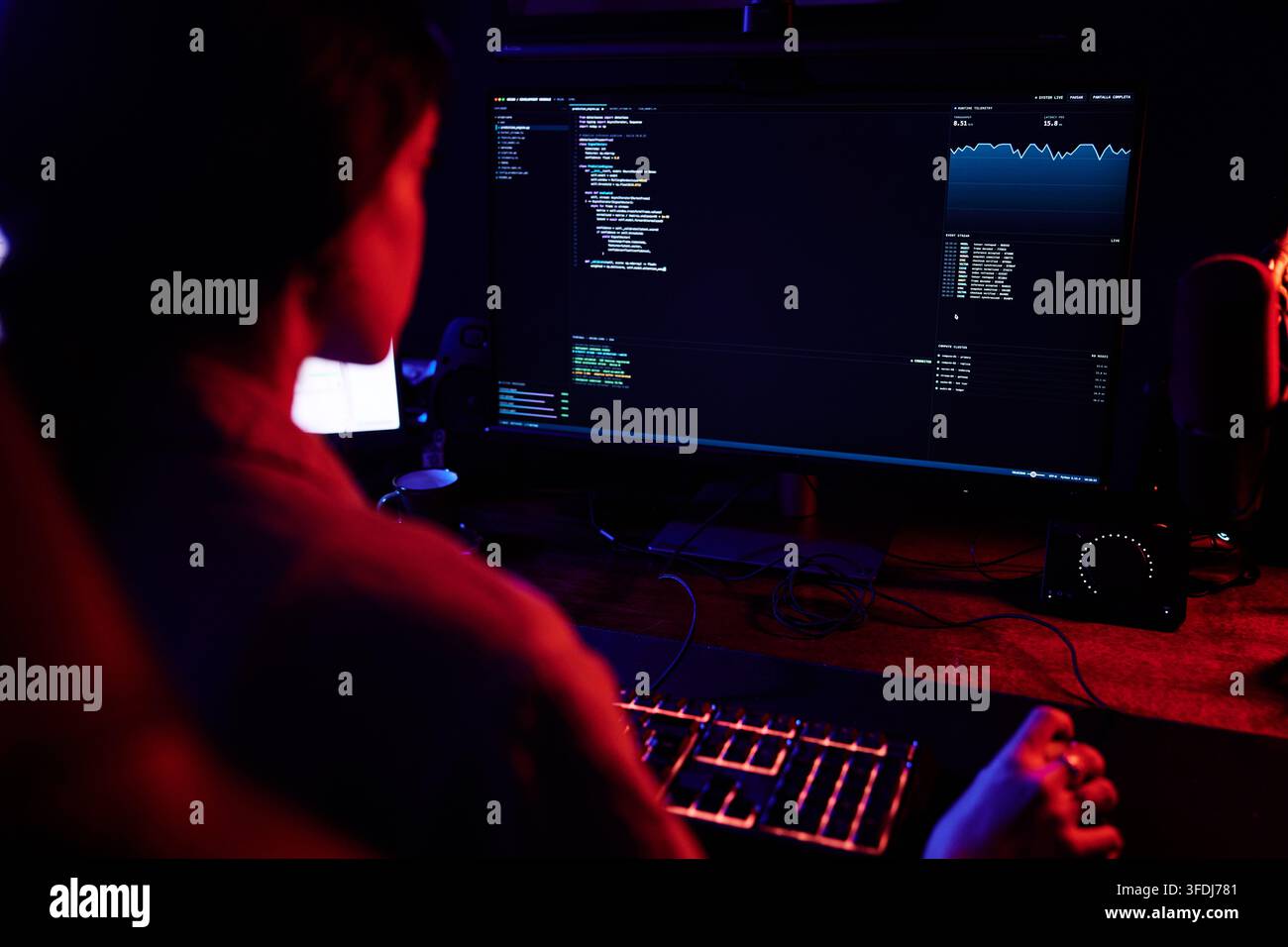 Hacker working on computer in dark room, writing code for cybersecurity attack or data breach, showing data on screen Stock Photo