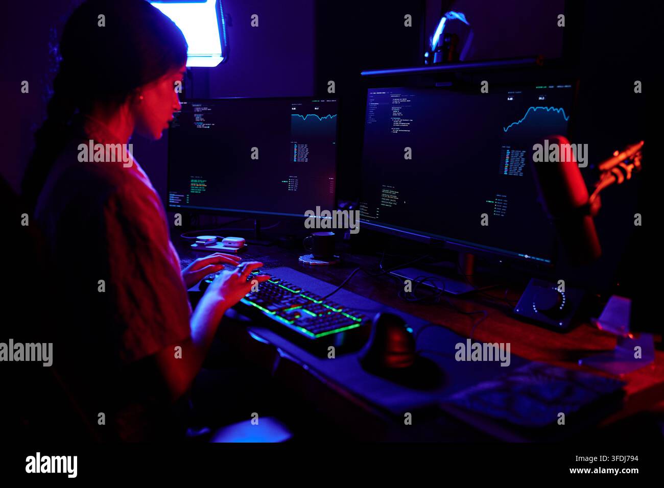 Woman programmer working on multiple computer screens with data and code, focusing on cybersecurity in a dark environment Stock Photo