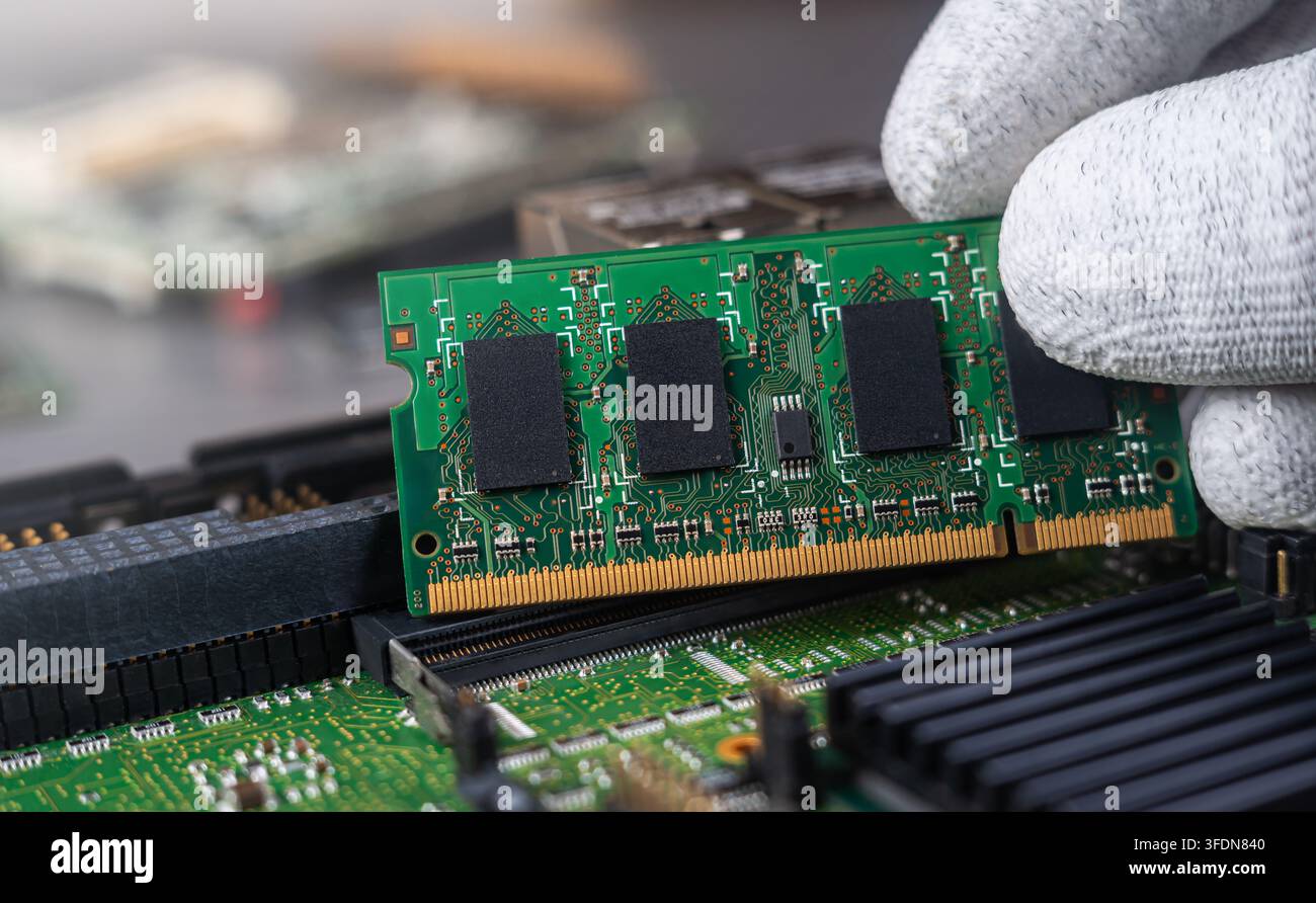 A person works on putting computer memory into a circuit board at a tech repair shop. Tools and other parts are visible in the workspace. Stock Photo