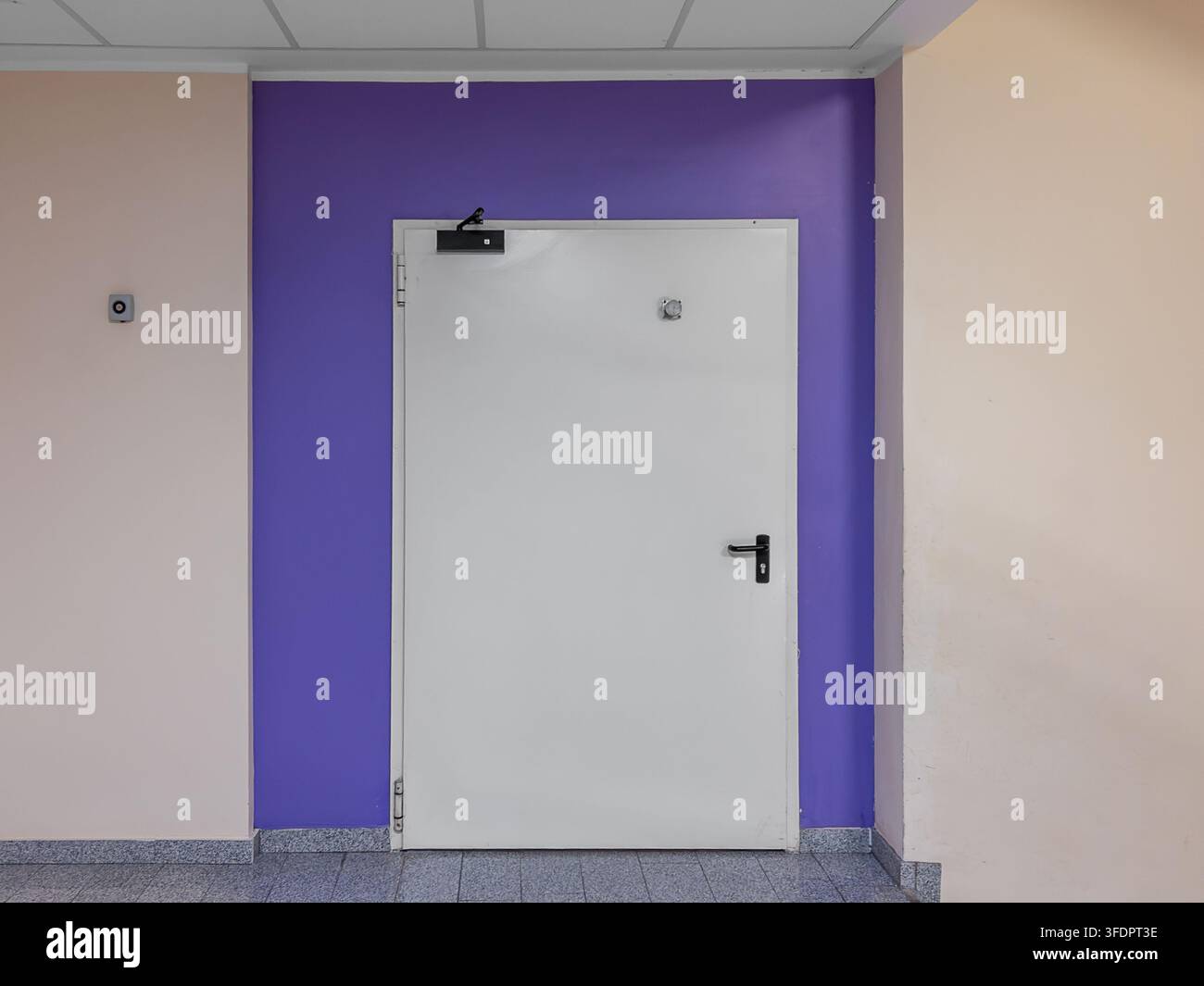 Single leaf white metal fire exit door with black handle and automatic closer hydraulic system installed on a purple painted wall section in a modern Stock Photo