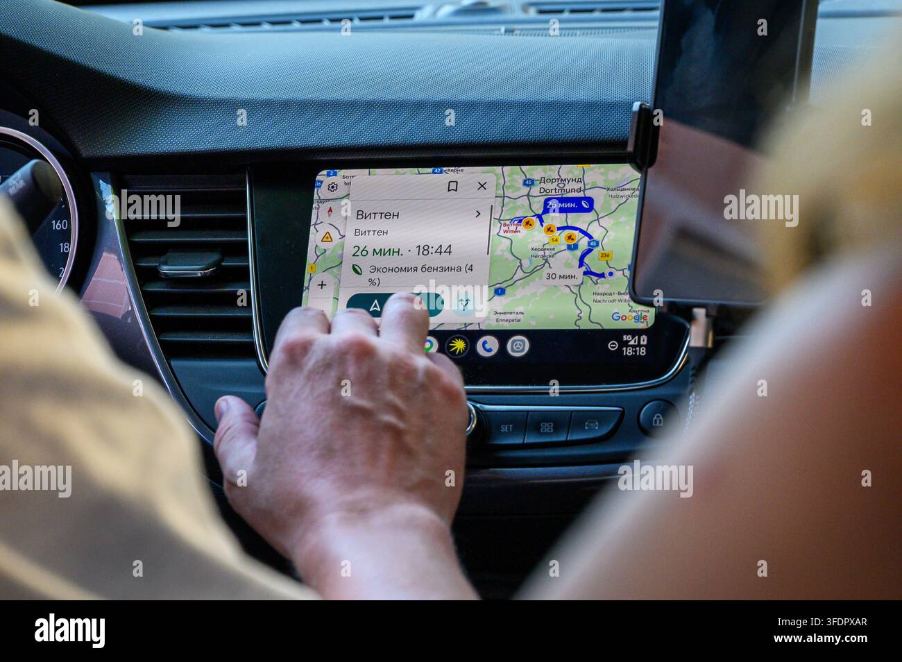 Iserlohn, Germany - August 13, 2026: Person's hand touching car infotainment screen displaying navigation map with routes. Stock Photo