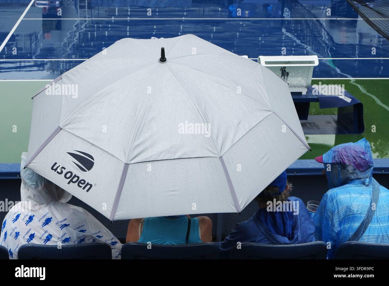 Spectators sit under an umbrella amid a rain delay during the first ...