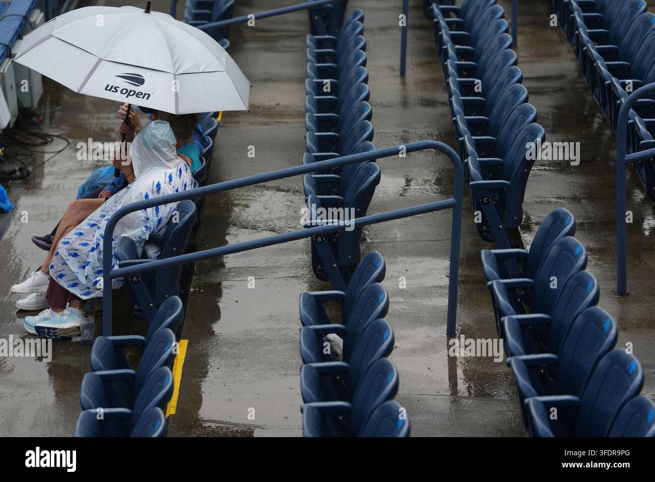 Spectators sit under an umbrella amid a rain delay during the first ...