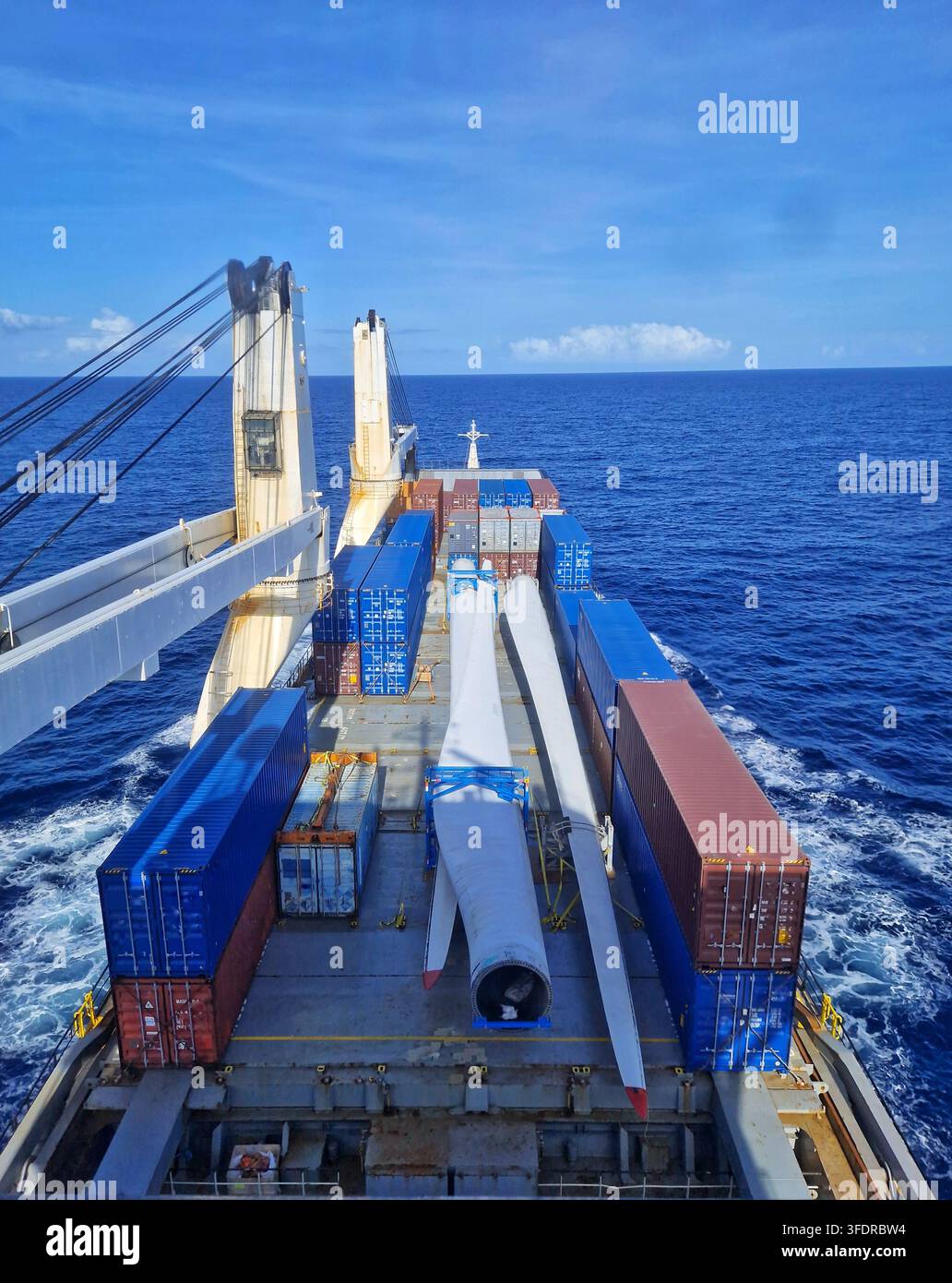 Cargo ship transporting giant wind turbine blades and freight containers on deck across the open sea for renewable energy project logistics - Smartphone Captured Stock Image