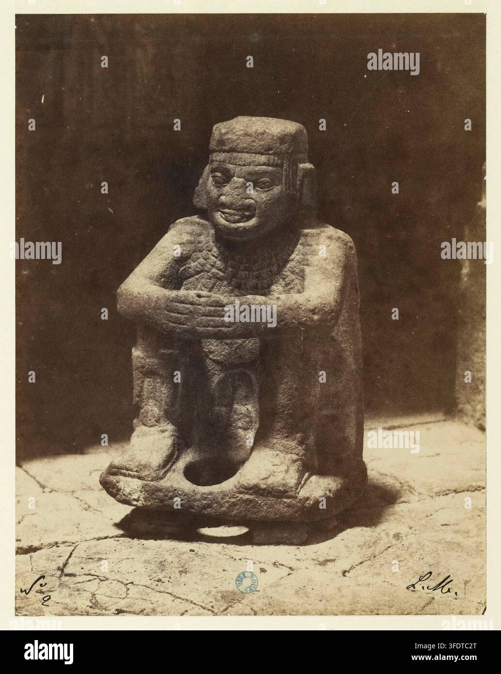 A stone sculpture of a seated Aztec warrior, depicted with arms crossed ...