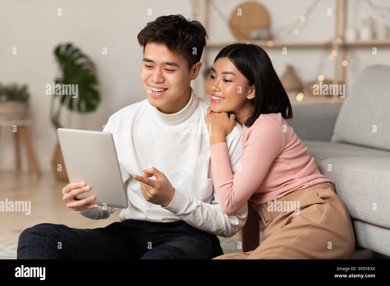 Young Asian Spouses Relaxing Using Digital Tablet Browsing Internet Indoors Stock Photo