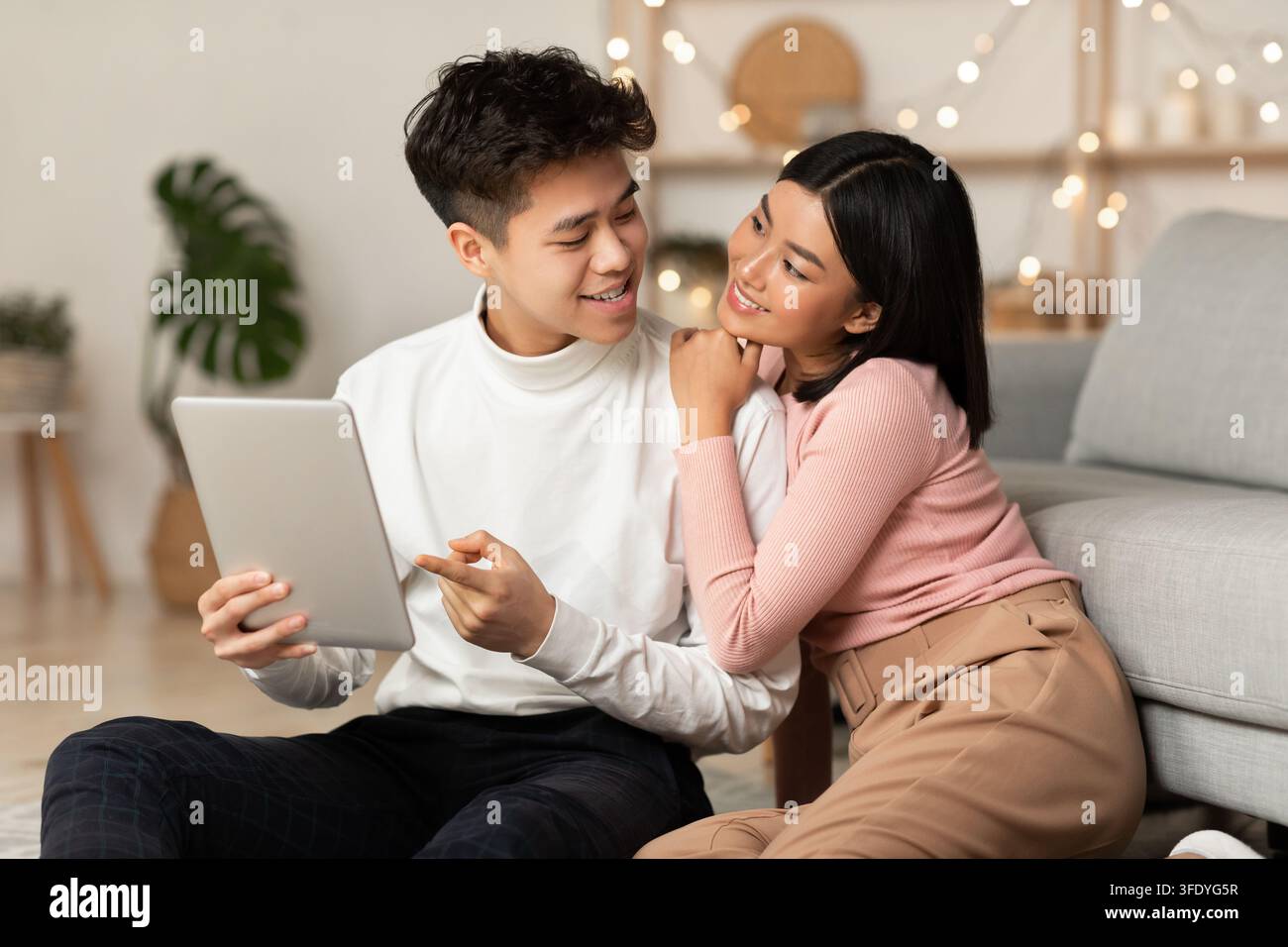 Asian Millennial Couple Using Digital Tablet Browsing Internet Indoors Stock Photo