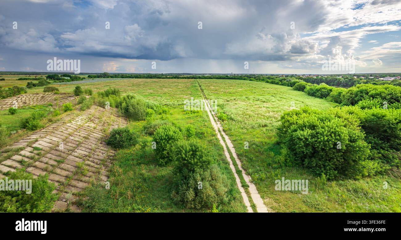 Vast green fields stretch under a dramatic sky. Winding path invites exploration through grassy terrain Stock Photo