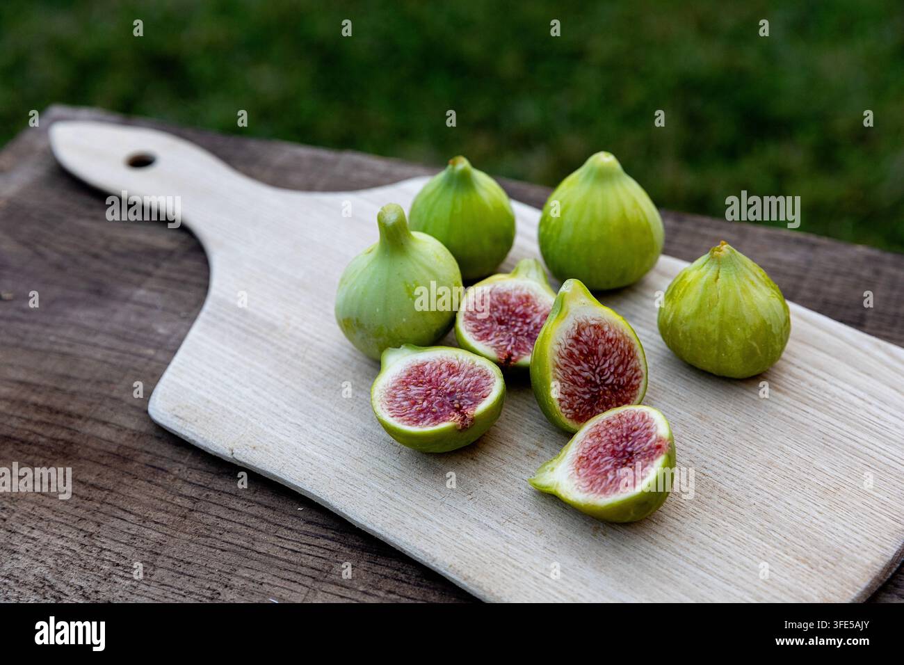 A beautiful rustic display of fresh figs, some whole and others sliced, beautifully arranged on a weathered wooden board for food styling. Stock Photo