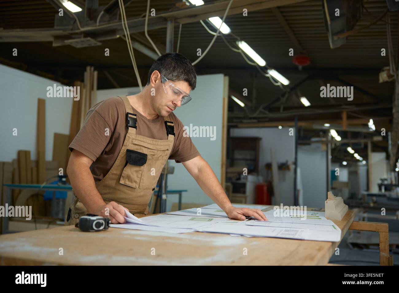 Workman assessing construction drawings in workshop while using measuring instruments and tools Stock Photo