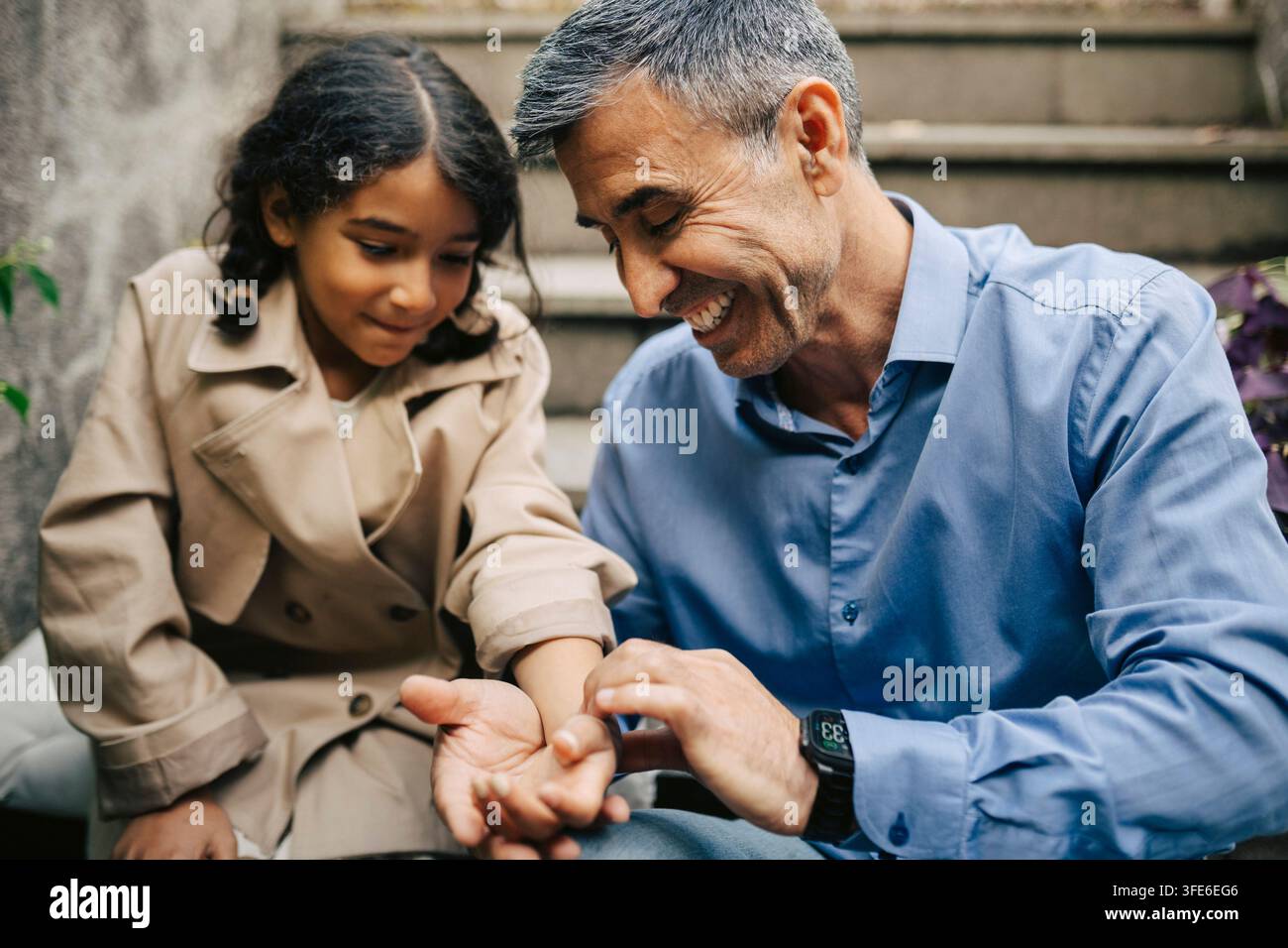 Happy senior man playing with his granddaughter while sitting on stairs Stock Photo