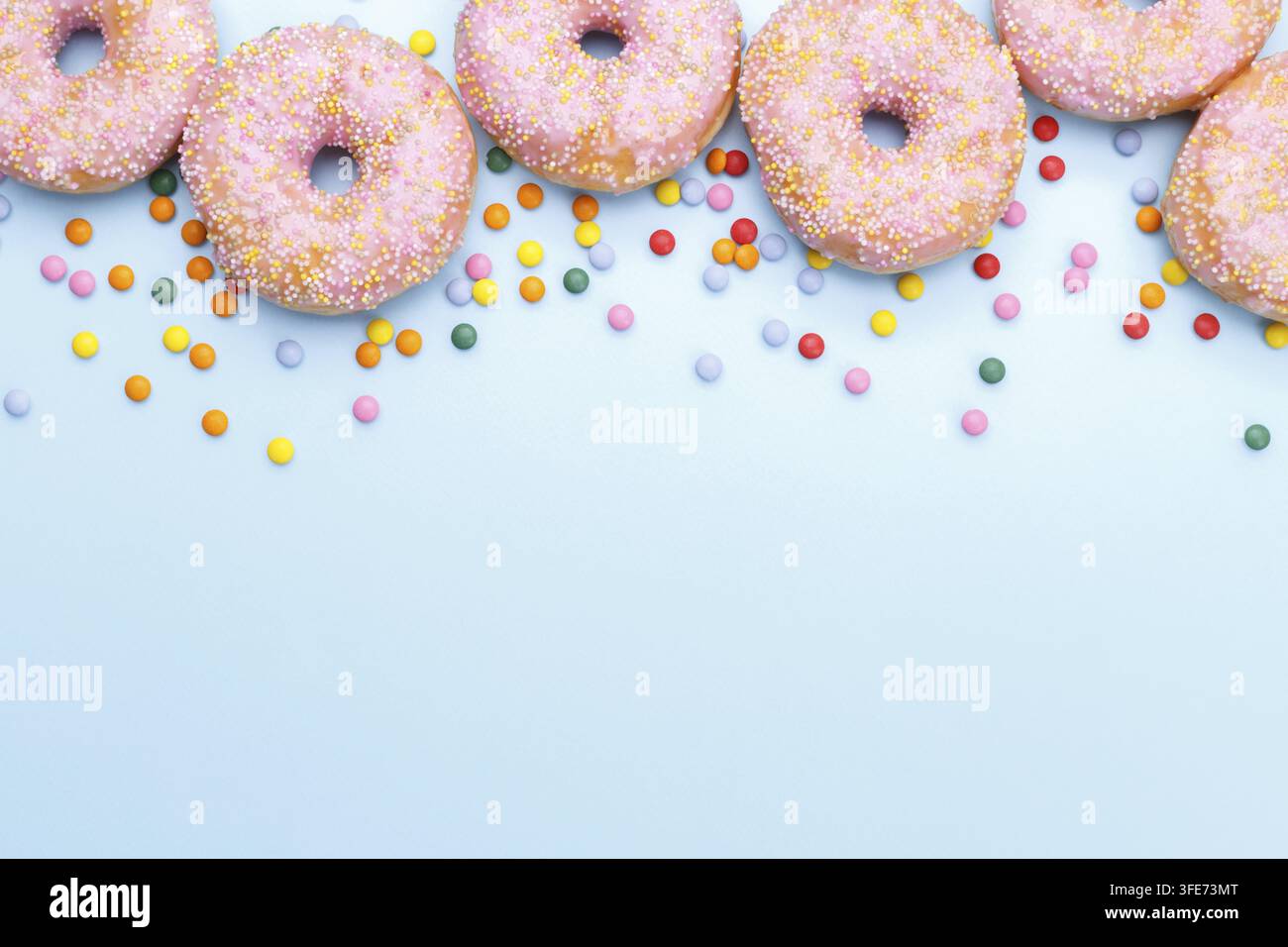 Pink doughnuts and candies on blue background, copy space flat lay Stock Photo