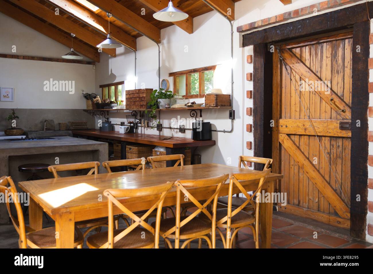 Wooden dining table with six crossback chairs is sitting in sunlit rustic kitchen Stock Photo