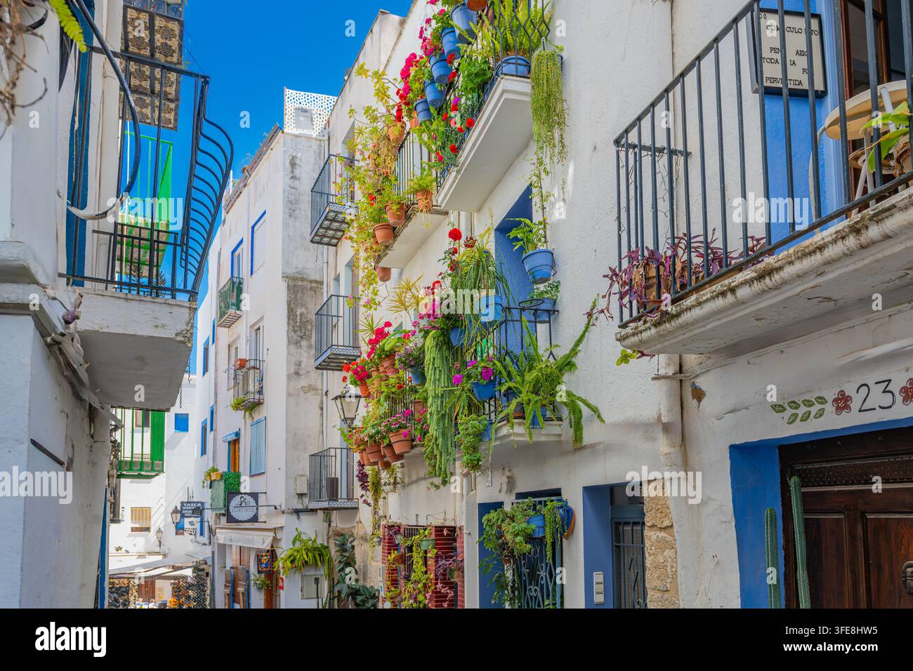 Low-angle view of flower-draped balconies and cascading potted plants on whitewashed houses in Peñíscola, Spain. Stock Photo