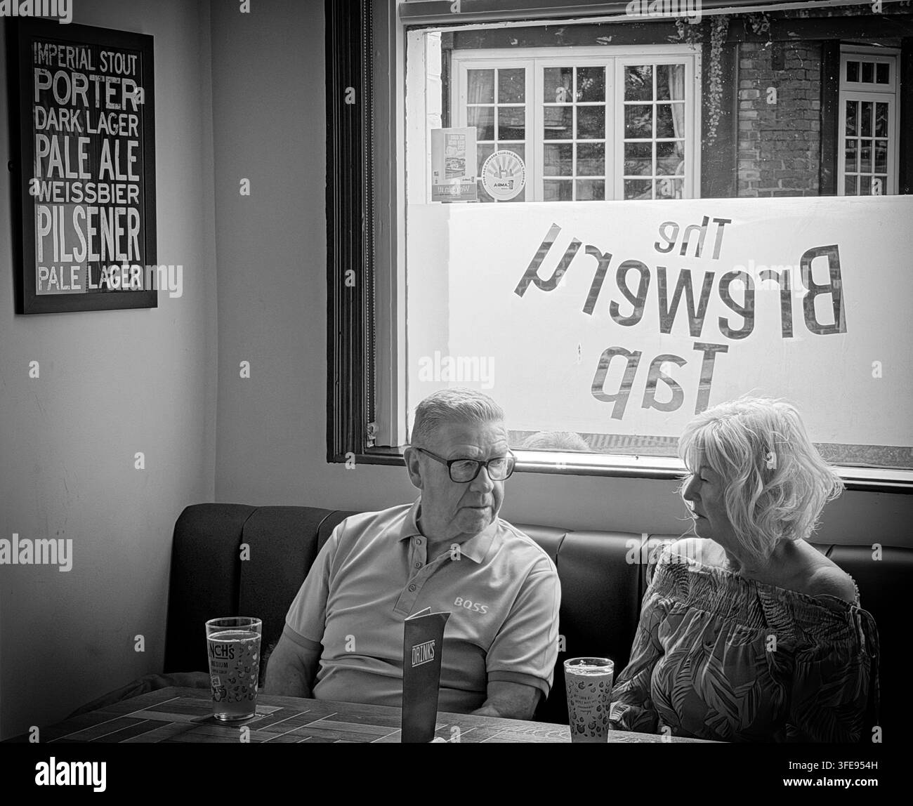 Traditional British hospitality scene. Couple relaxing with drinks inside a pub, the Lymm brewery tap, photographed in black and white. Stock Photo