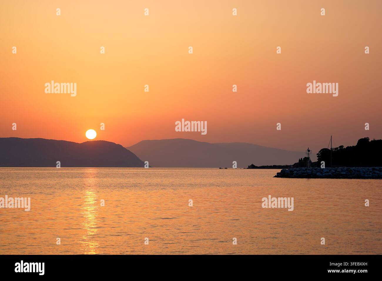 Sun Setting Behind Hills Over a Calm Sea Stock Photo