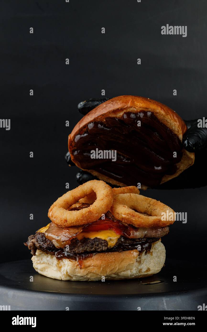 Hand placing saucy bun on loaded burger Stock Photo