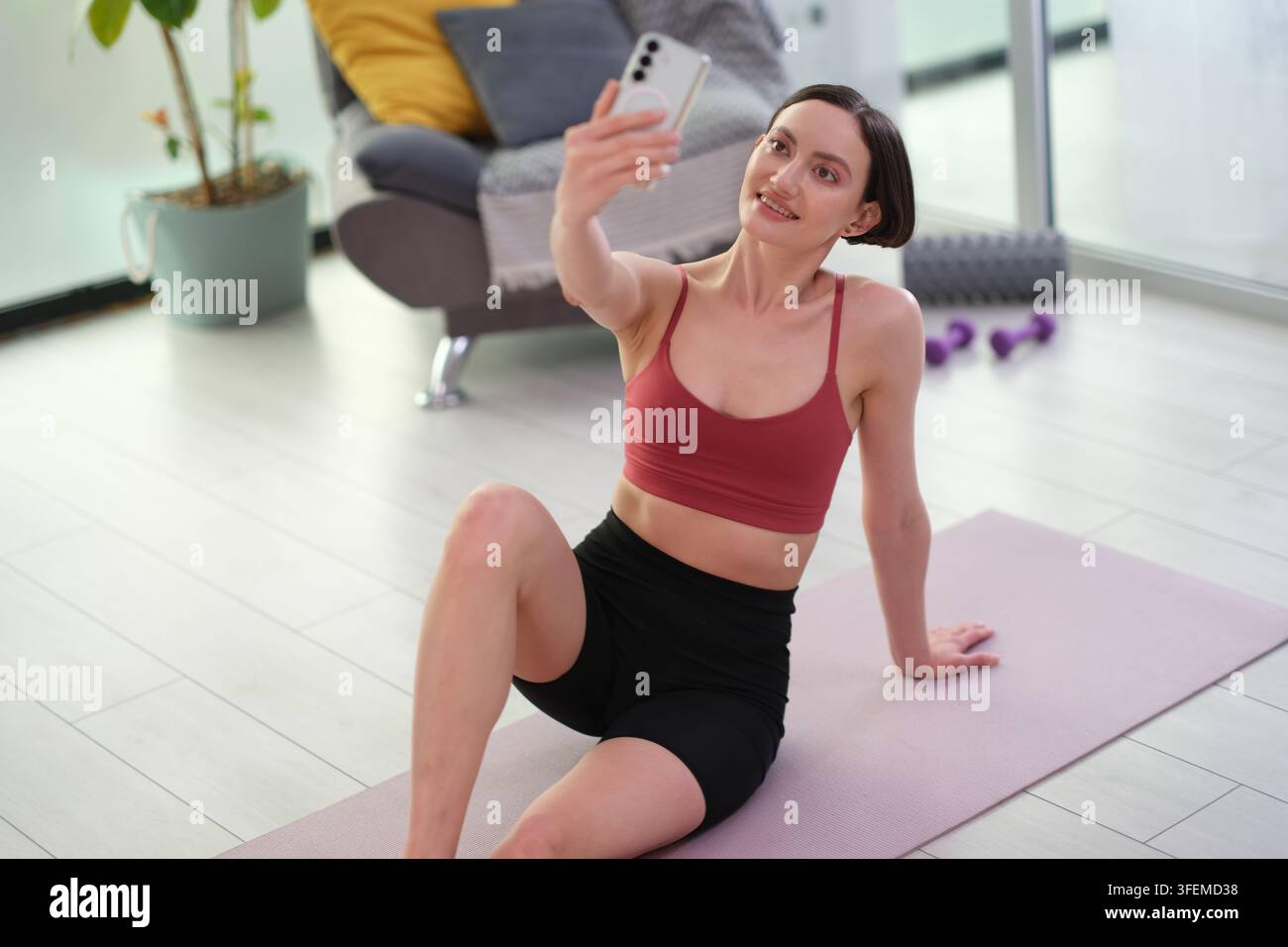 Pretty woman in activewear takes selfie by smartphone at home gym Stock Photo