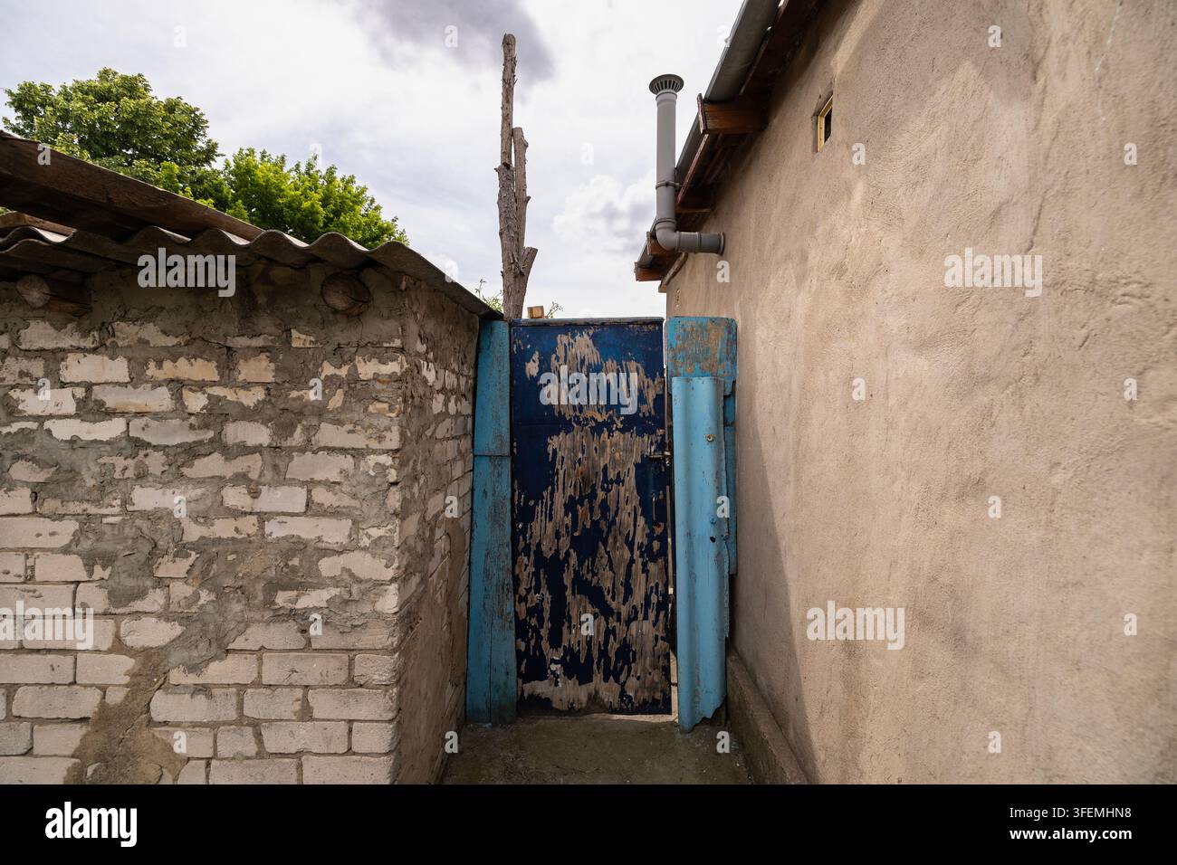 Old weathered blue wooden door between rustic buildings under a cloudy sky Stock Photo