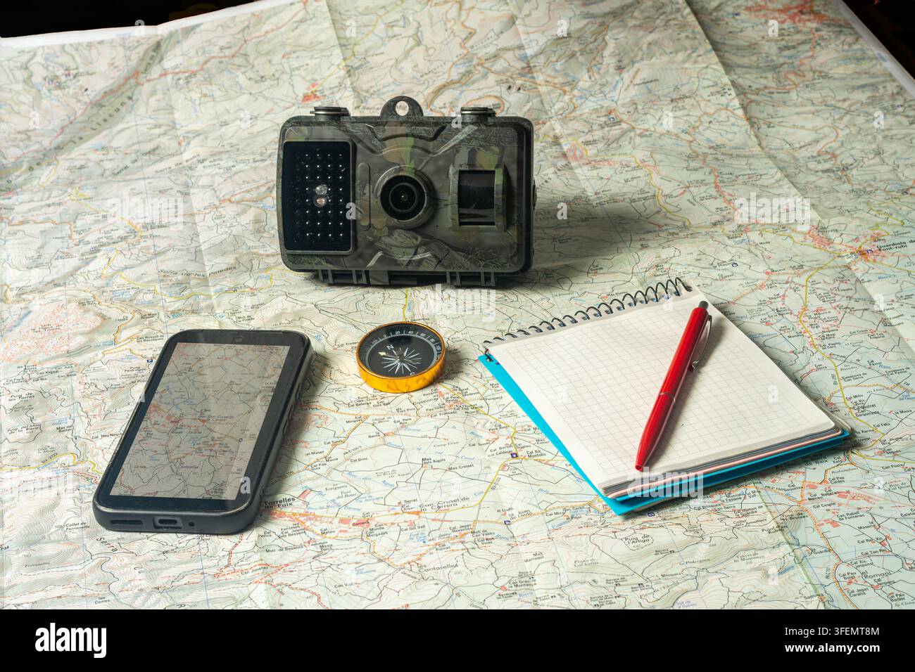 Trail camera, compass, smartphone and notebook on map for exploration Stock Photo