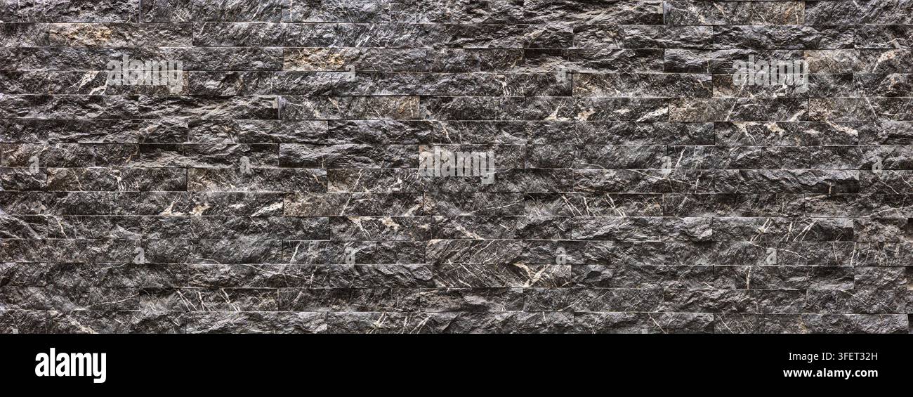 Dark gray marble tiles creating a rough textured stacked stone wall pattern Stock Photo