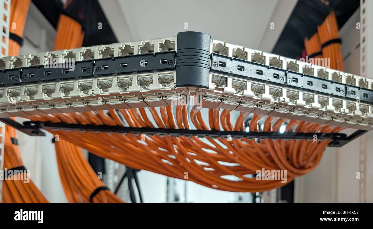 Close-up of network patch panels and organised orange data cabling inside a communications rack, showing structured cabling infrastructure. Stock Photo