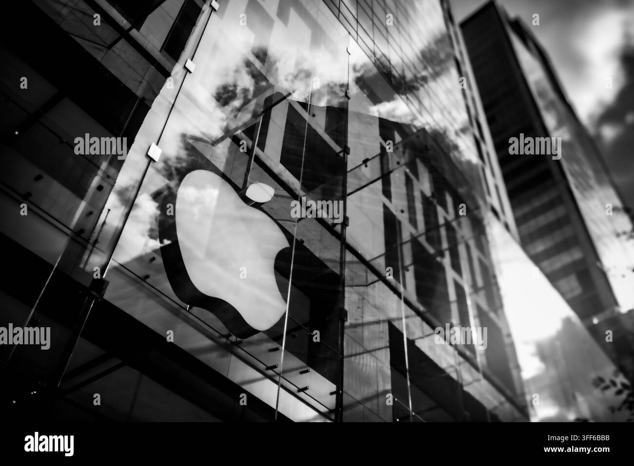 Monochrome shot of the iconic Apple corporate logo on the structural glass facade of a modern retail flagship store. Stock Photo