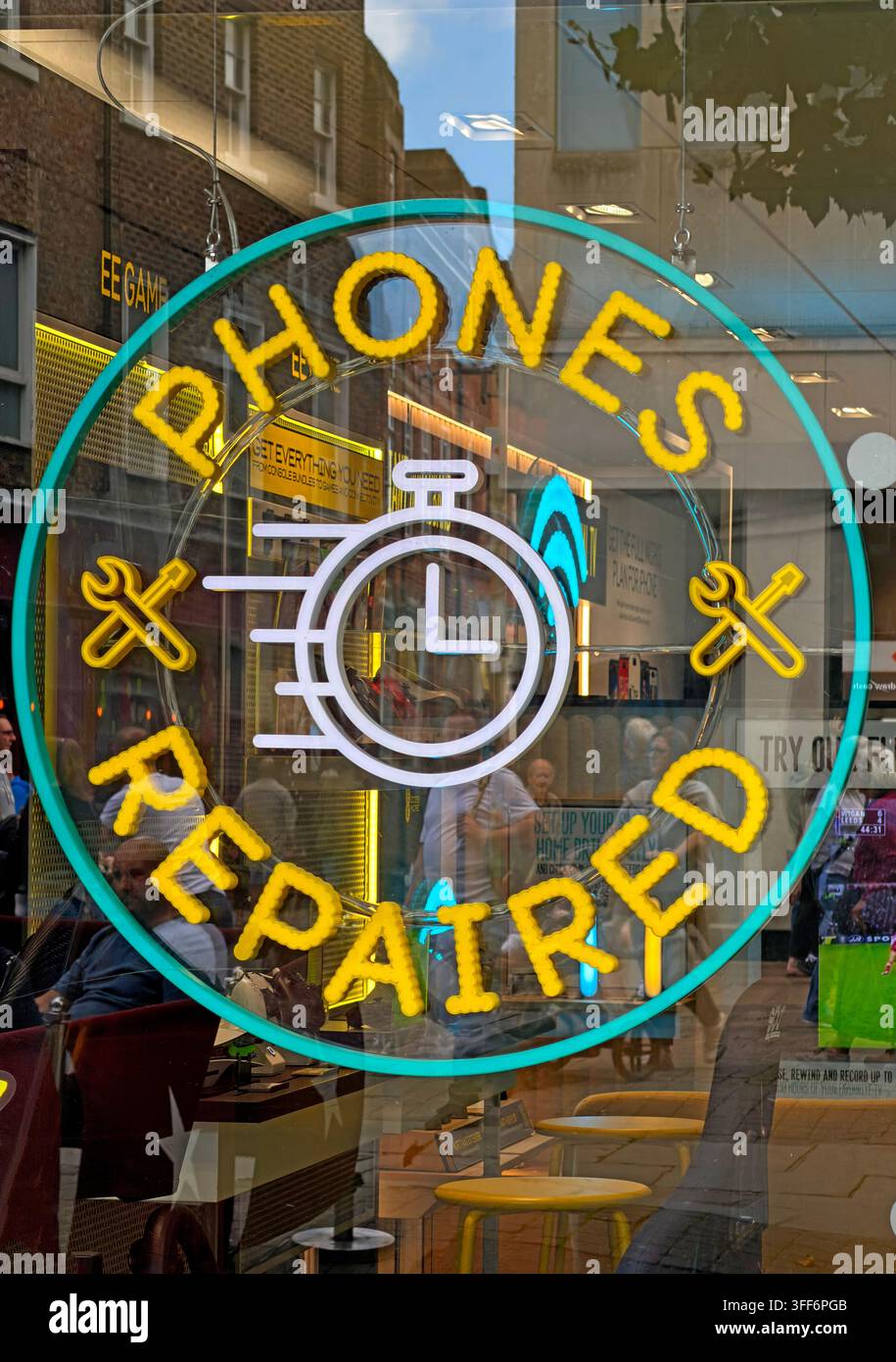 Neon 'Phones Repaired' sign in a mobile phone shop window, advertising high-street repair services beside an EE retailer. Stock Photo
