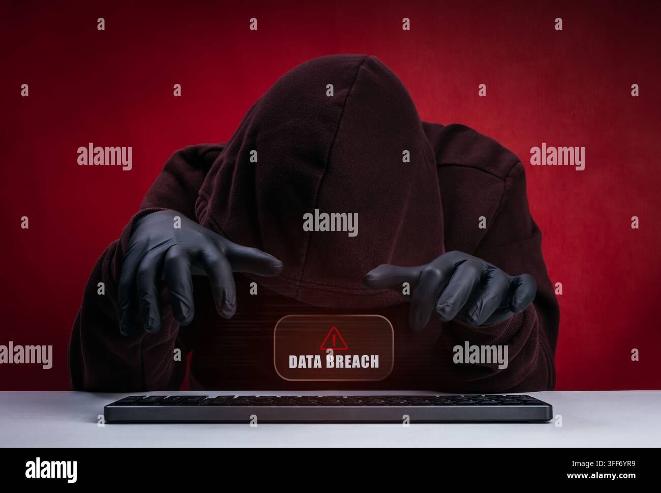 Hooded hacker wearing black gloves using keyboard computer during data breach. Cyberattack, unauthorized access, information theft, security threats, Stock Photo