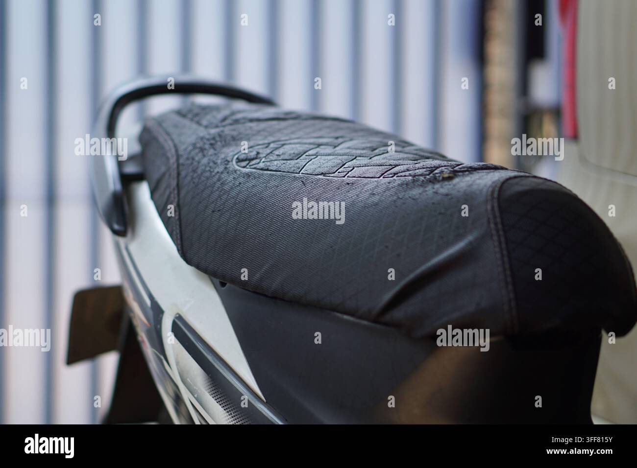 A detailed close-up showing a worn black leather motorcycle seat featuring visible scratches and scuffs in a garage setting. Stock Photo