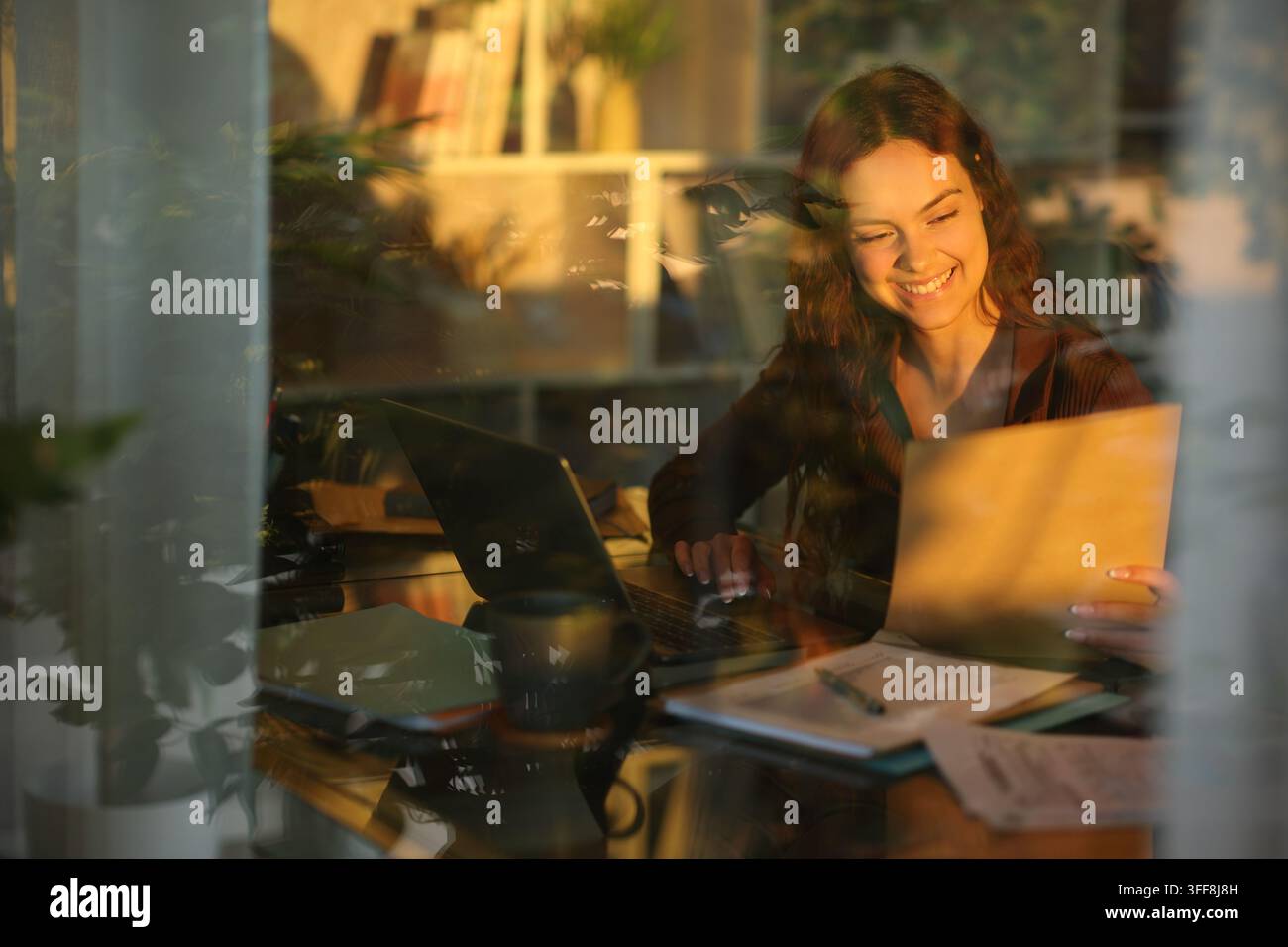 Happy telecommuter working checking documents at home viewed through a window Stock Photo